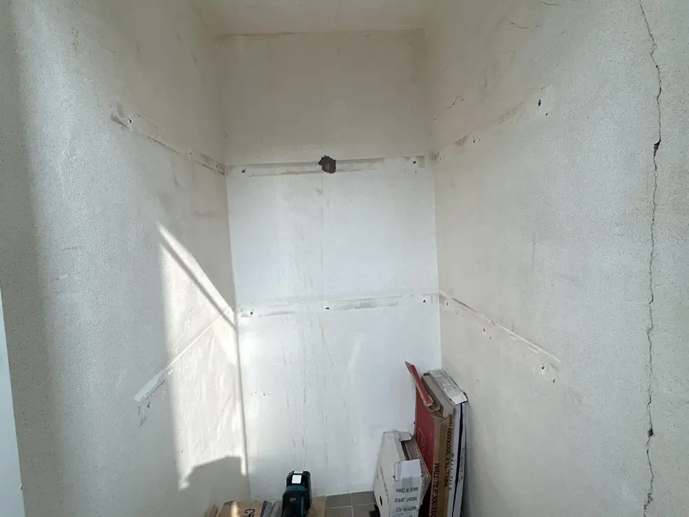베란다 벽 균열 보수 작업 후 — 선반을 걷어낸 뒤 벽에 남은 자국과 세로 균열이 보이는 상태